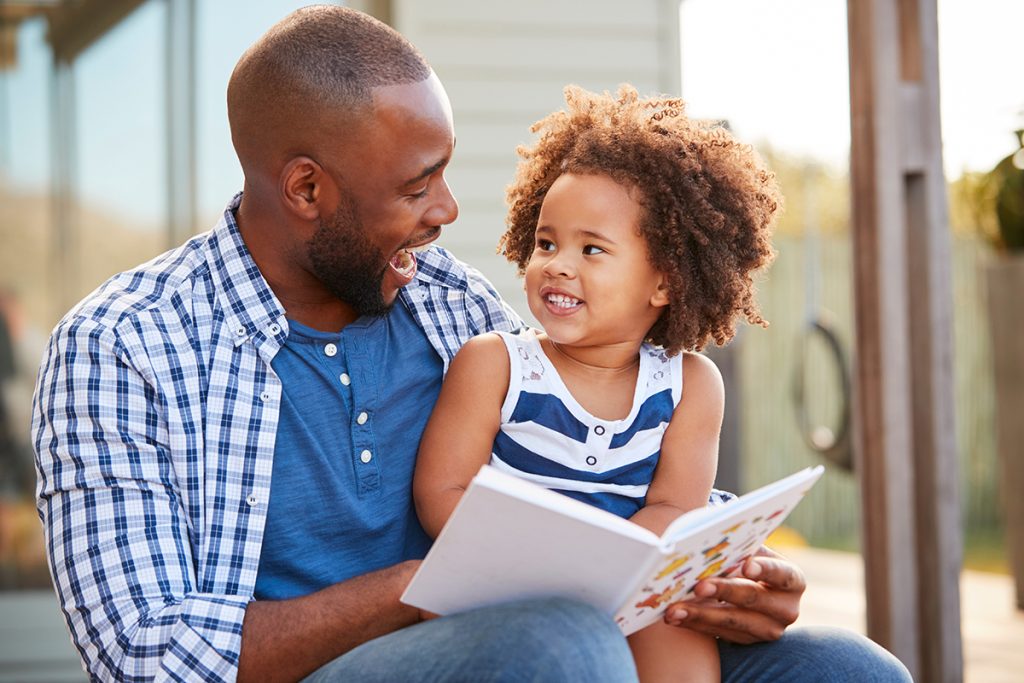 Man with young daughter reading book on house stair